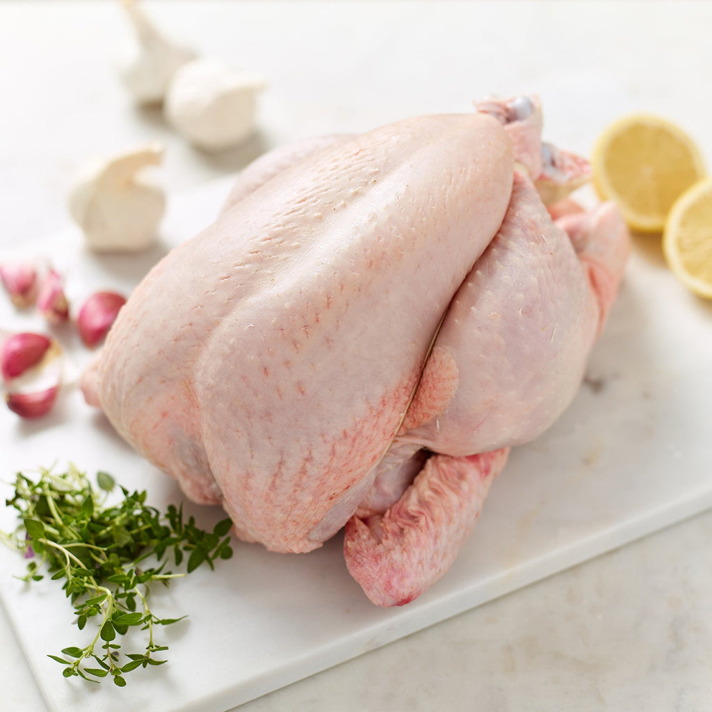 Organic whole chicken with lemon halves, garlic bulbs and segments and thyme
